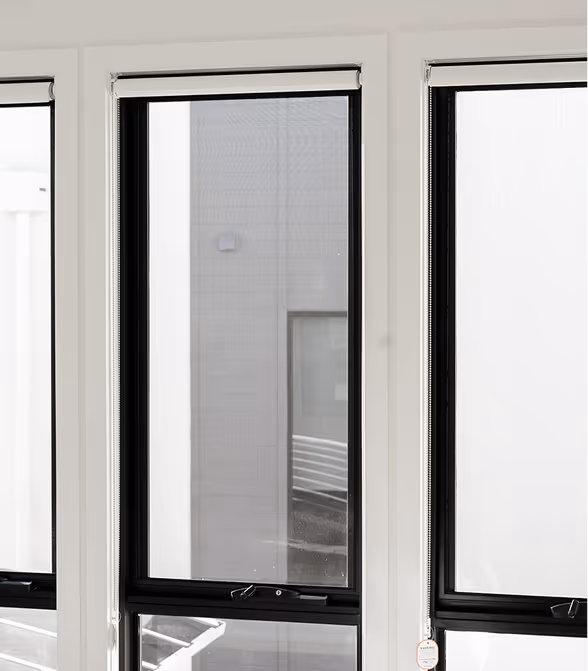 Three large windows with black frames and white walls reflecting part of a neighboring building.