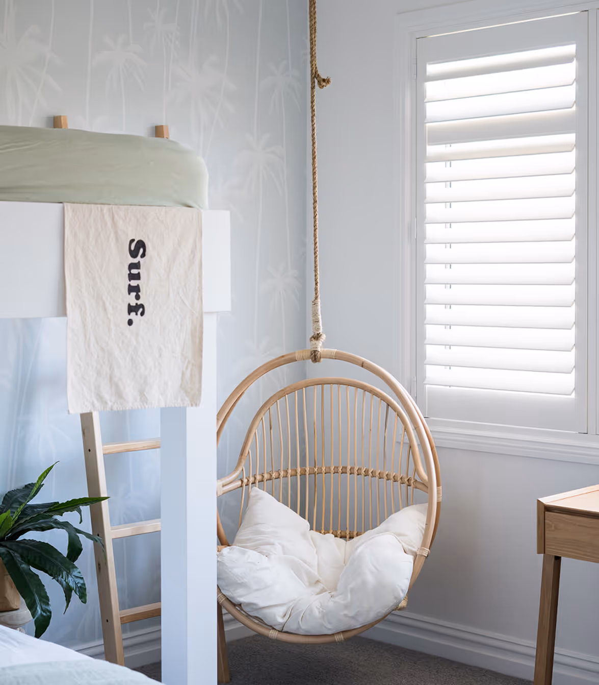Minimalist bedroom corner with a hanging rattan chair, white cushion, potted plant, and bunk bed.