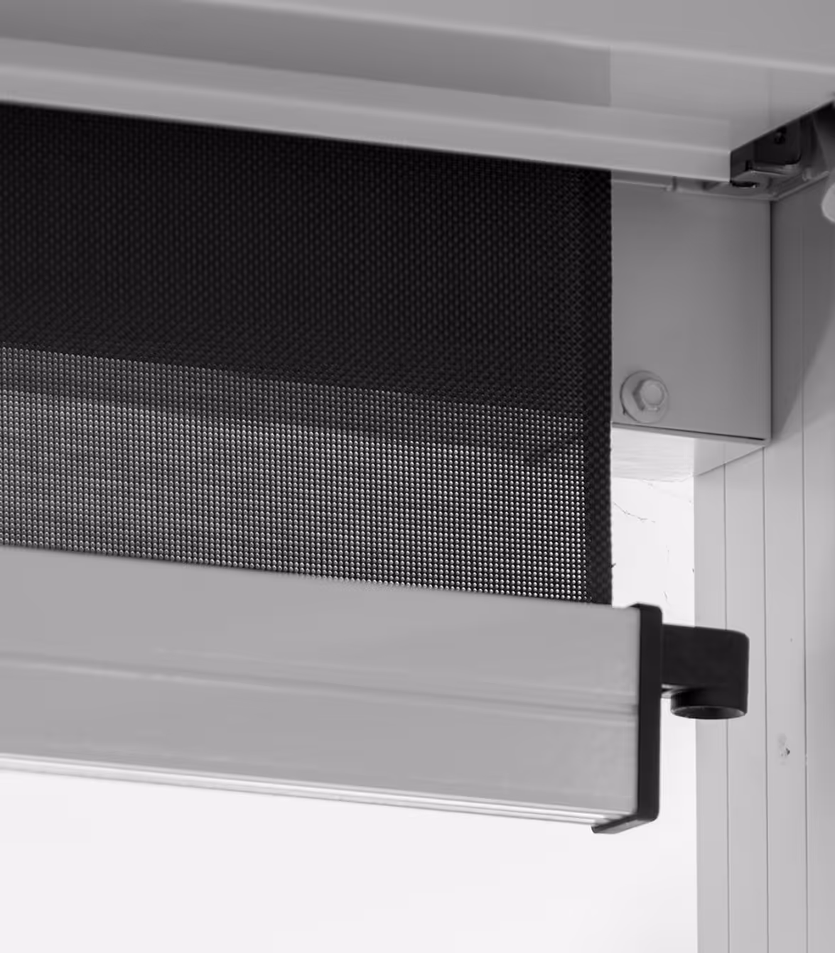 Close-up of a retractable black mesh sunshade or screen mounted on a white window frame.