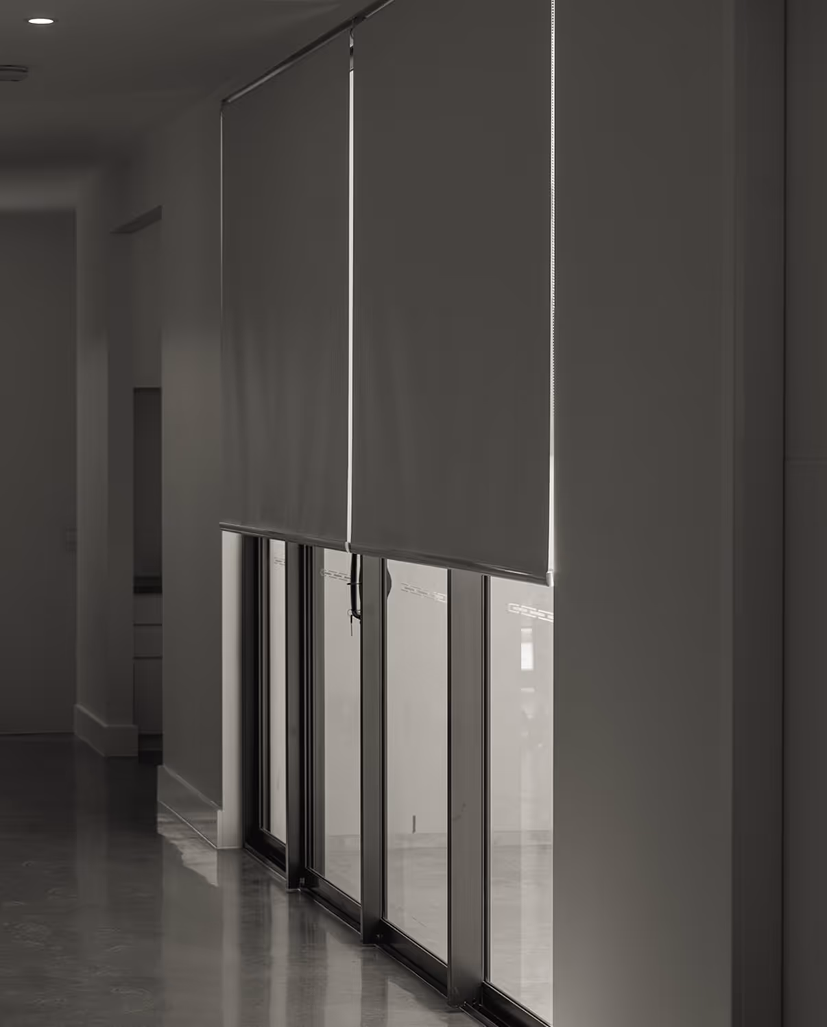 Modern window blinds partially covering glass doors in a dimly lit hallway with polished floor.