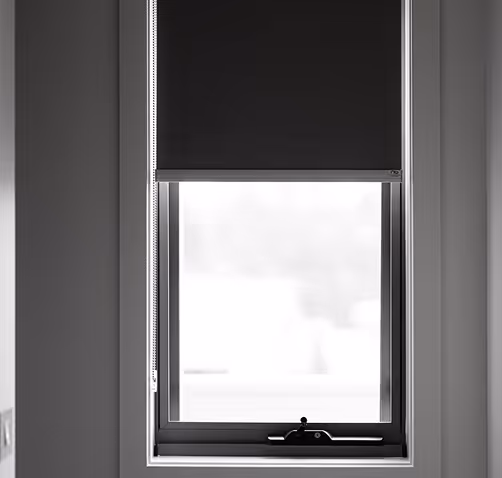 Window with half-lowered black roller blind and white walls around it.