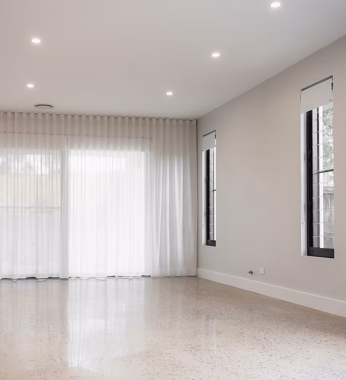 Empty modern room with polished terrazzo floor, sheer curtain, two narrow windows with roller blinds.