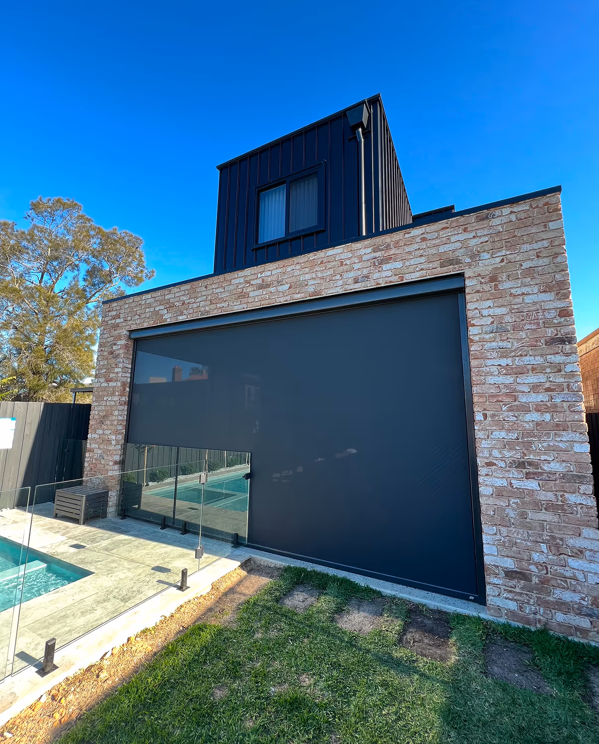 Modern house with brick facade and black retractable outdoor screen beside glass pool fence.