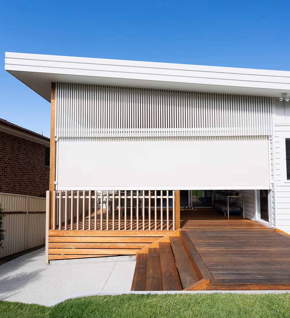 Modern white retractable awning shading a wooden porch attached to a house under clear blue sky.