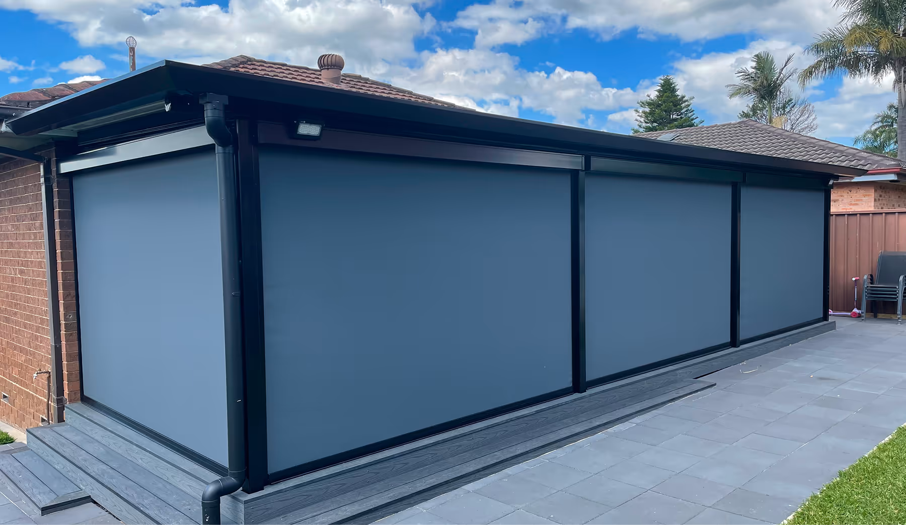 Modern outdoor patio with retractable gray fabric awnings on a black frame and tiled flooring.