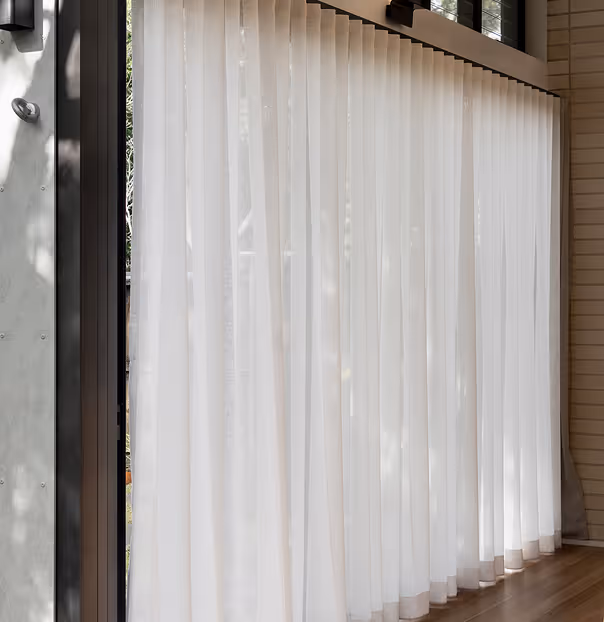 White wave fold sheer curtains hanging in front of large modern glass door with wooden floor.