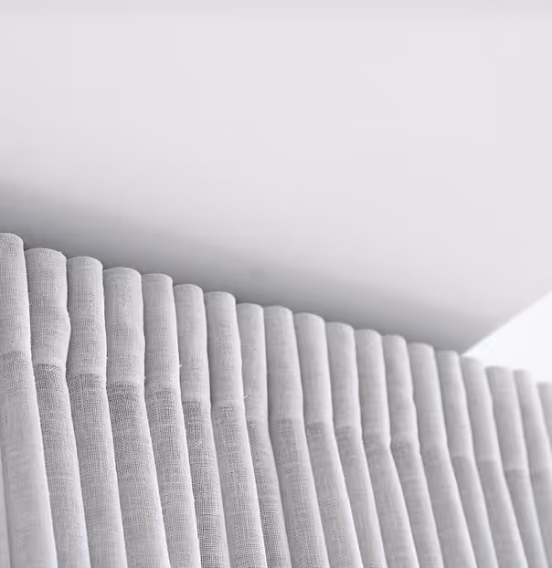 Close-up of white sheer curtains hanging in uniform, soft folds.