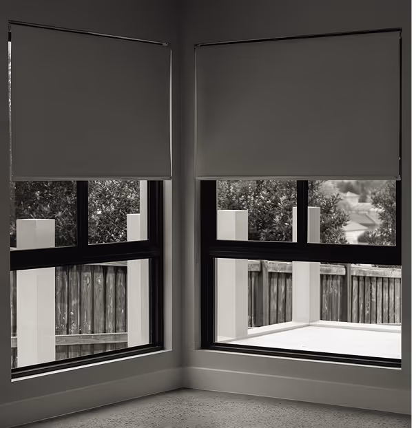 Two corner windows with partially lowered gray roller blinds and outdoor fence and trees visible.