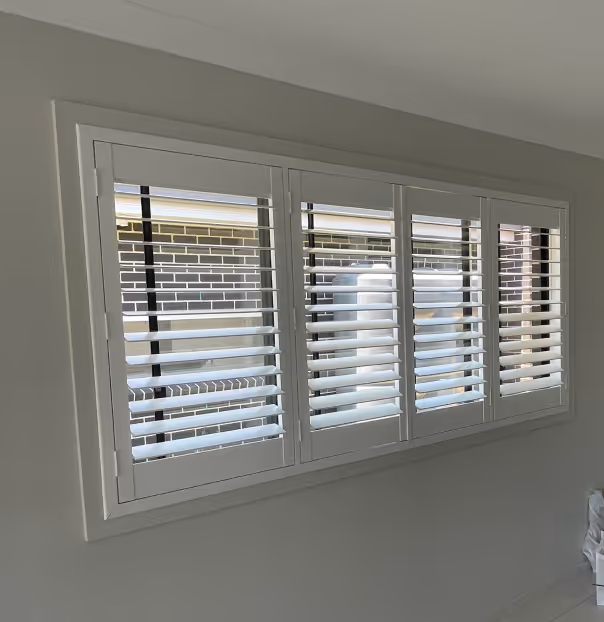 White interior window shutters partially open, showing a brick wall outside.
