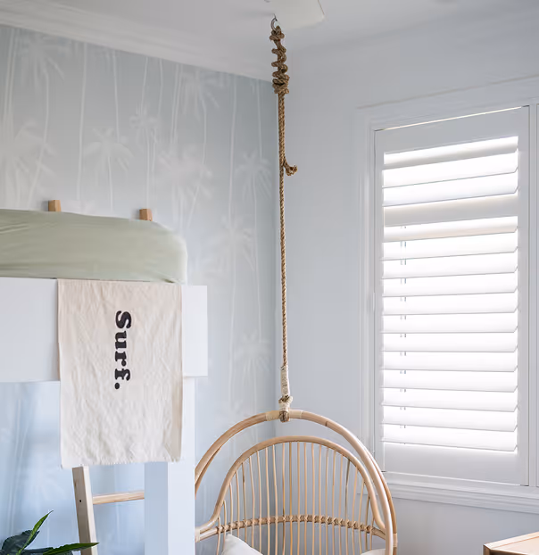 Bright room corner with a white bunk bed, hanging rattan chair, and window with white shutters.
