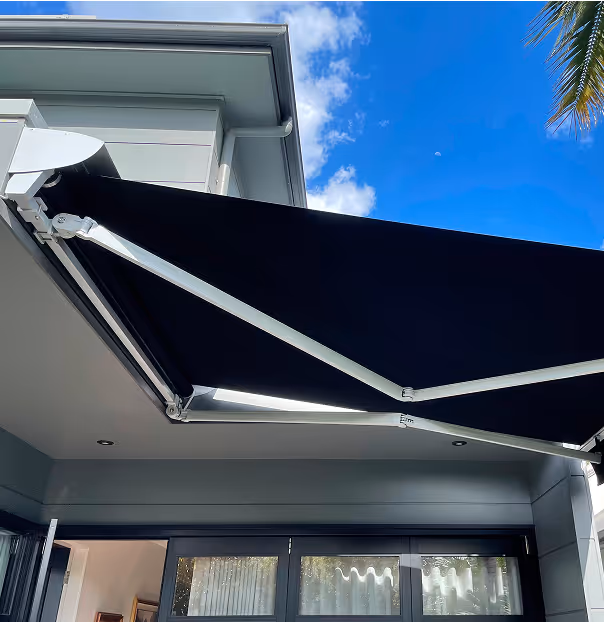 Black retractable awning extended over patio doors on a modern house under a blue sky.