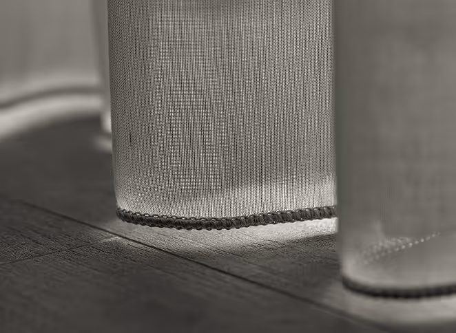 Close-up of sheer curtains hanging just above a wooden floor with light filtering through.