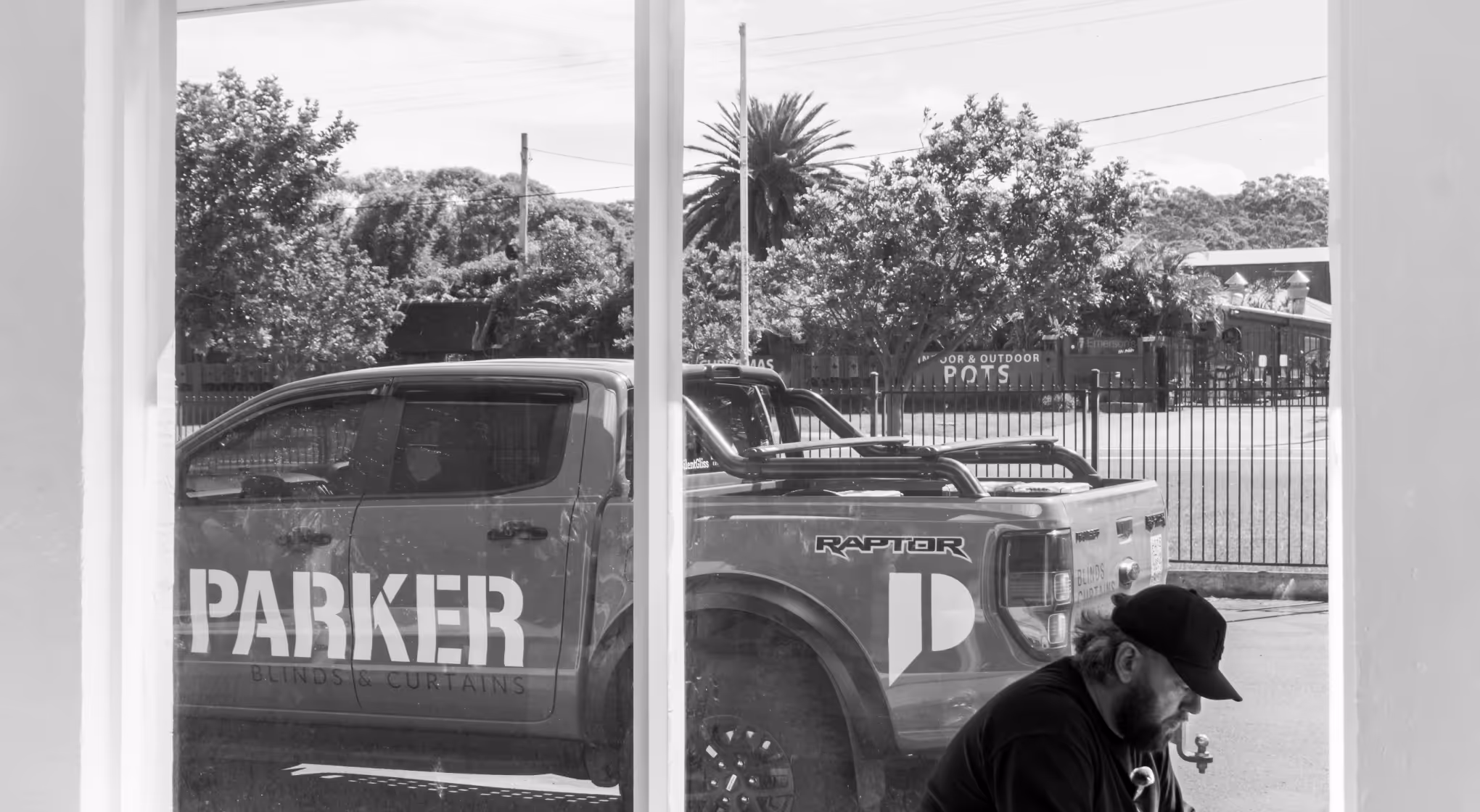 Man wearing a cap sitting near window with a Parker Blinds & Curtains branded pickup truck outside.