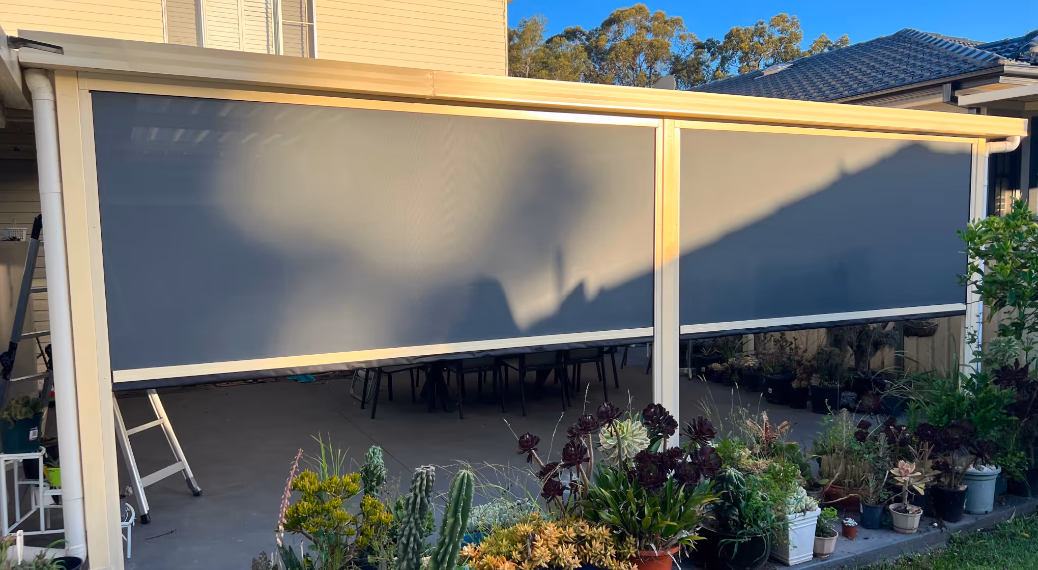 Outdoor patio with a beige retractable sunshade blocking the view of furniture and plants.