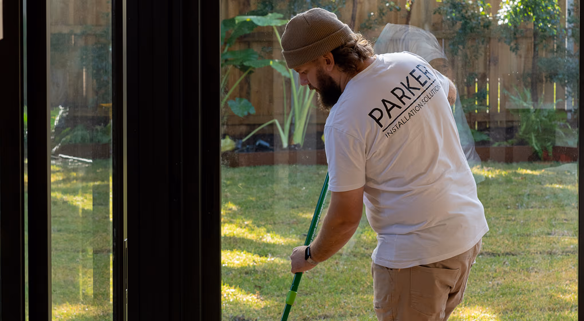 Man in a Parker Installations Solutions shirt cleaning glass door or window with a green mop.