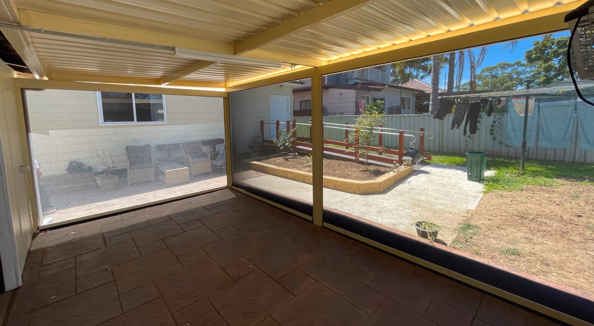Covered patio with screen walls overlooking a garden bed and backyard with laundry hanging to dry.
