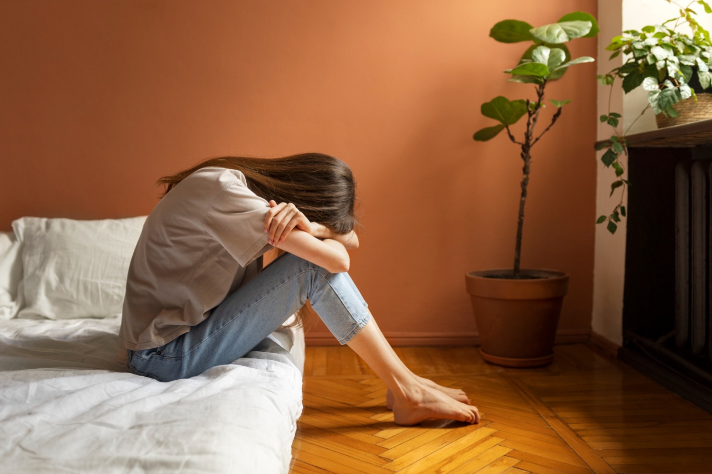Person sitting alone on a bed with their head down, reflecting feelings of emotional distress, loneliness, or the need for a safe space to share emotions.