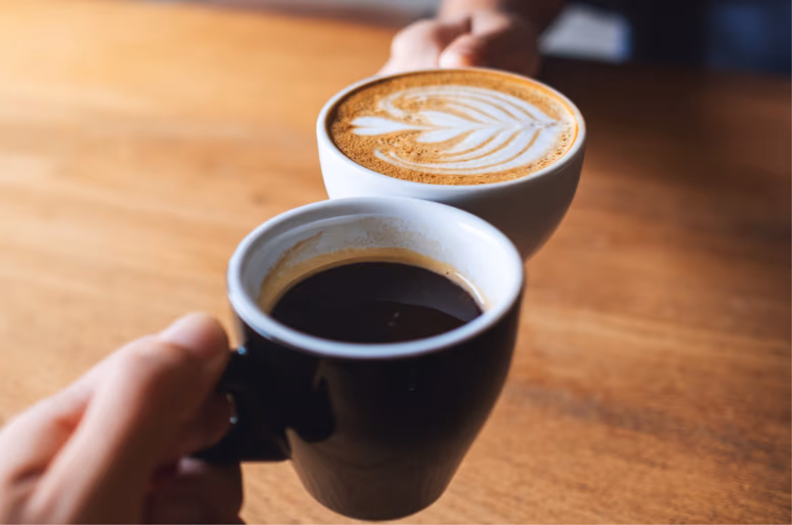 Zwei Hände stoßen zwei Kaffeetassen an.