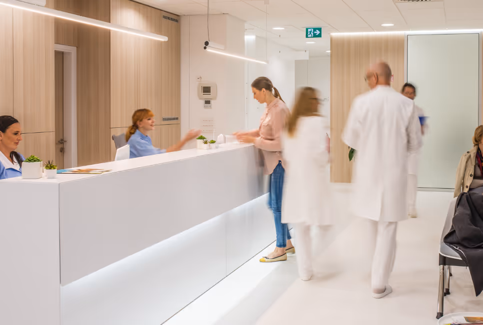 Empfangsbereich einer modernen Arztpraxis mit Patientin, medizinischem Personal und laufendem Praxisbetrieb
