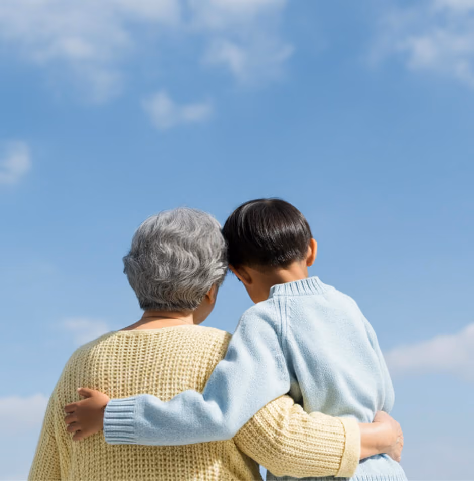 Grandparent and child embracing with arms around each other under blue sky.