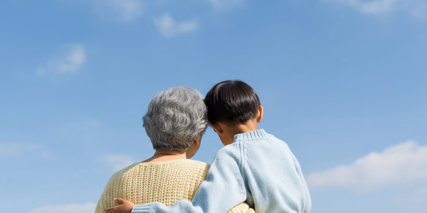 Child with dark hair wearing light blue sweater hugging an older person with gray hair and yellow sweater.