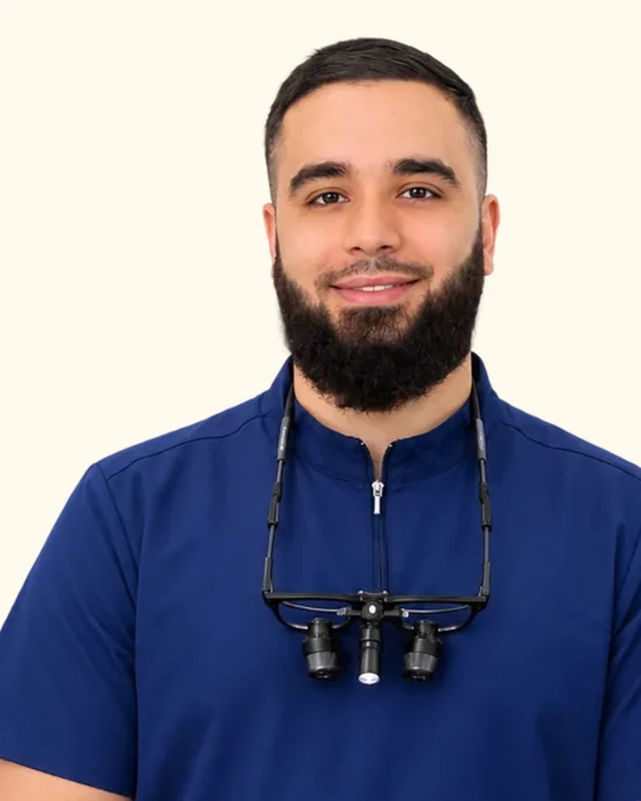 Nadim Elhami at Berala Dental, in navy clinical scrubs with dental loupes.