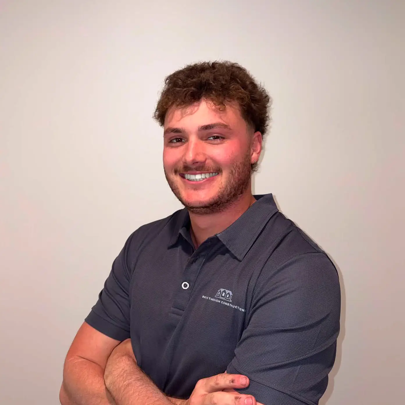 Smiling man with curly hair and beard wearing a gray polo shirt against plain background.