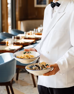 Waiter in white jacket holding plates of pasta and mussels in a restaurant
, Mr. C Miami – Coconut Grove, luxury hotel.
