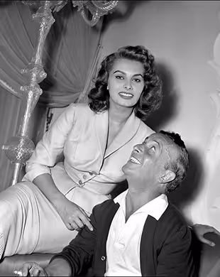 Smiling woman in light outfit sitting behind smiling man in dark cardigan in black-and-white photo, Mr. C Miami – Coconut Grove, luxury hotel.