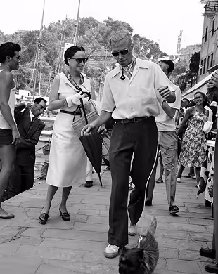 Man wearing sunglasses walks a small dog while a woman in a dress smiles nearby on a busy street
, Mr. C Miami – Coconut Grove, luxury hotel.