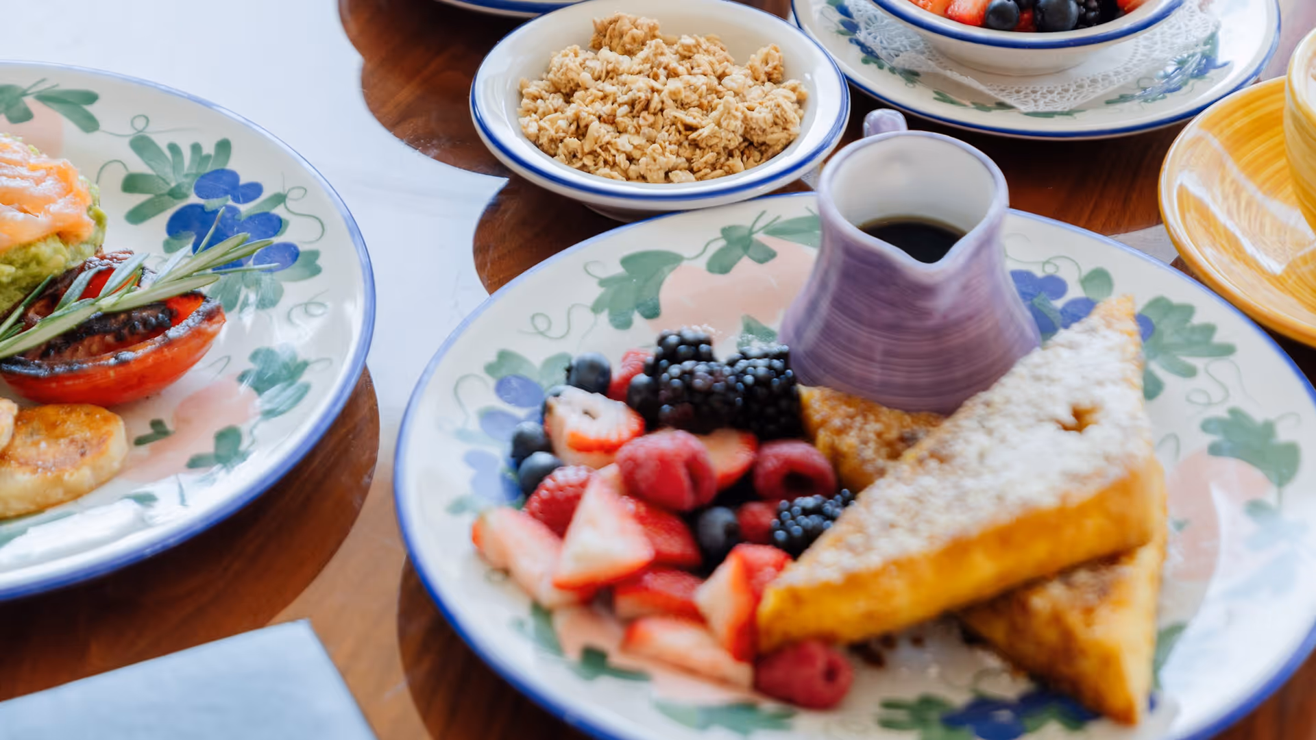 Assiettes avec fruits frais, pain grillé en poudre, granola, tomates grillées et plat d'avocat sur une table en bois.