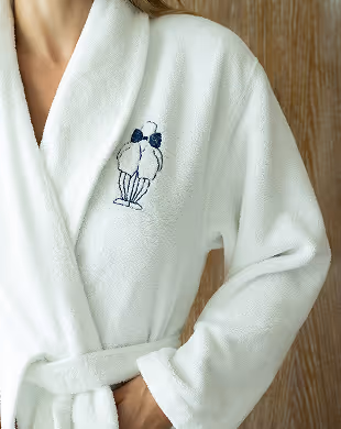 Person wearing a white robe with an embroidered cocktail glass and bow tie design on the chest, Mr. C Miami – Coconut Grove, luxury hotel.