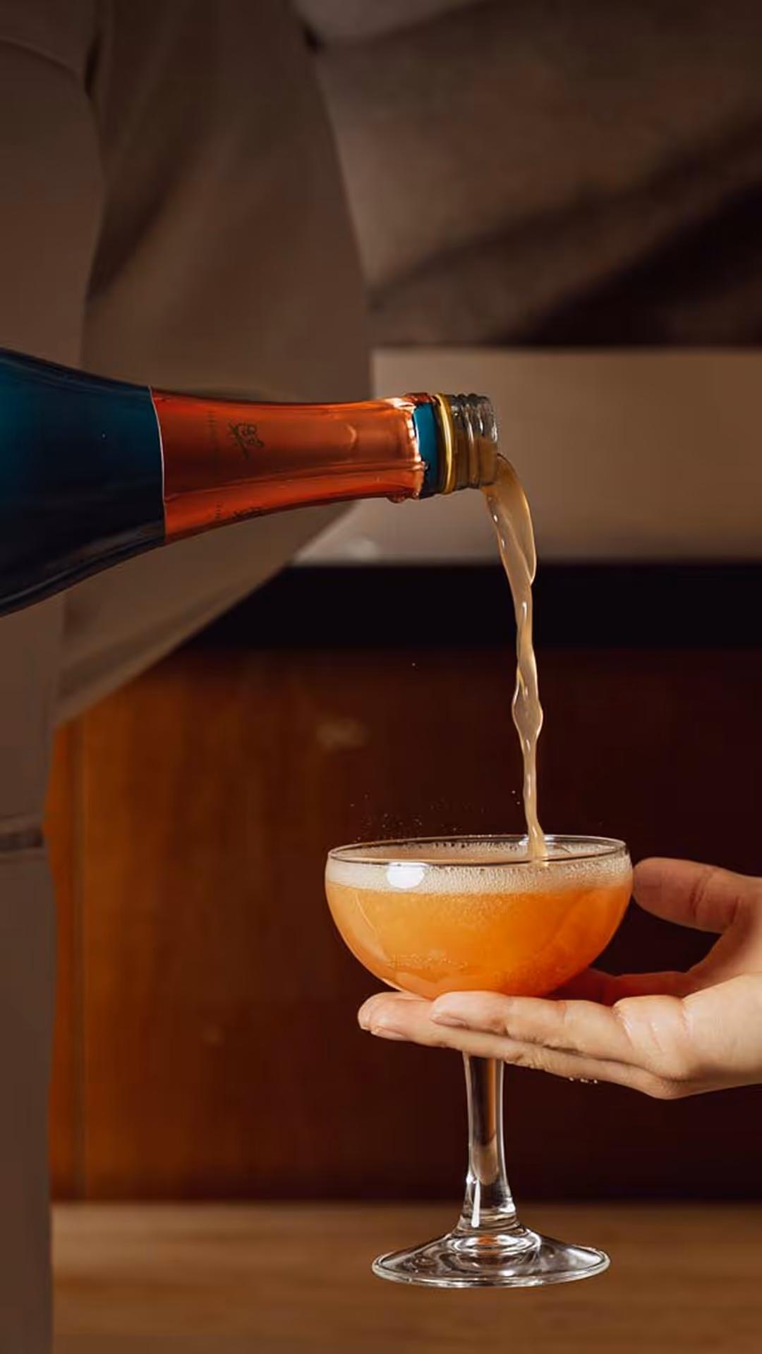 Hand holding a coupe glass as amber liquid is poured from a bottle into it against a warm background
, Mr. C Miami – Coconut Grove, luxury hotel.