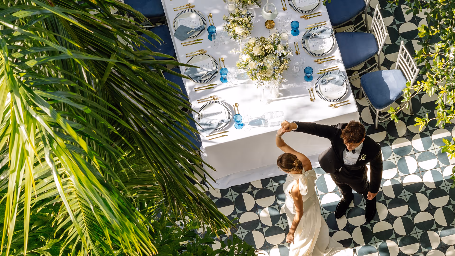 Bride and groom dancing on patterned floor near a decorated table with white flowers and blue glasses, Mr. C Miami – Coconut Grove, luxury hotel.