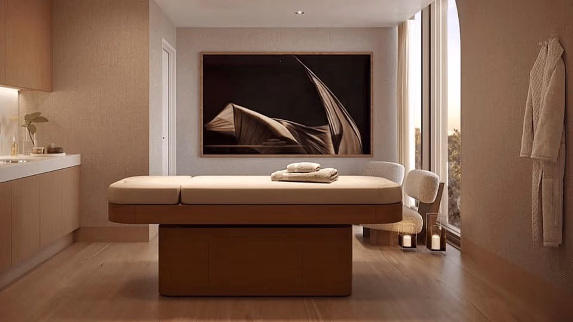 Sala spa minimalista con lettino da massaggio, asciugamani, due sedie, candele e una grande arte murale astratta.