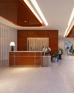 Moderna reception con pannelli in legno, lampada, piante e pavimento bianco lucido in una lobby luminosa.