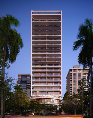 Alto edificio moderno con balconi curvi fiancheggiati da palme sotto il cielo blu al tramonto.