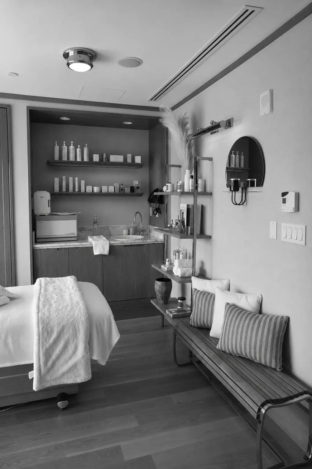 Sala de spa con mesa de masaje, banco de madera con cojines, estantes, lavabo y productos para el cuidado de la piel.