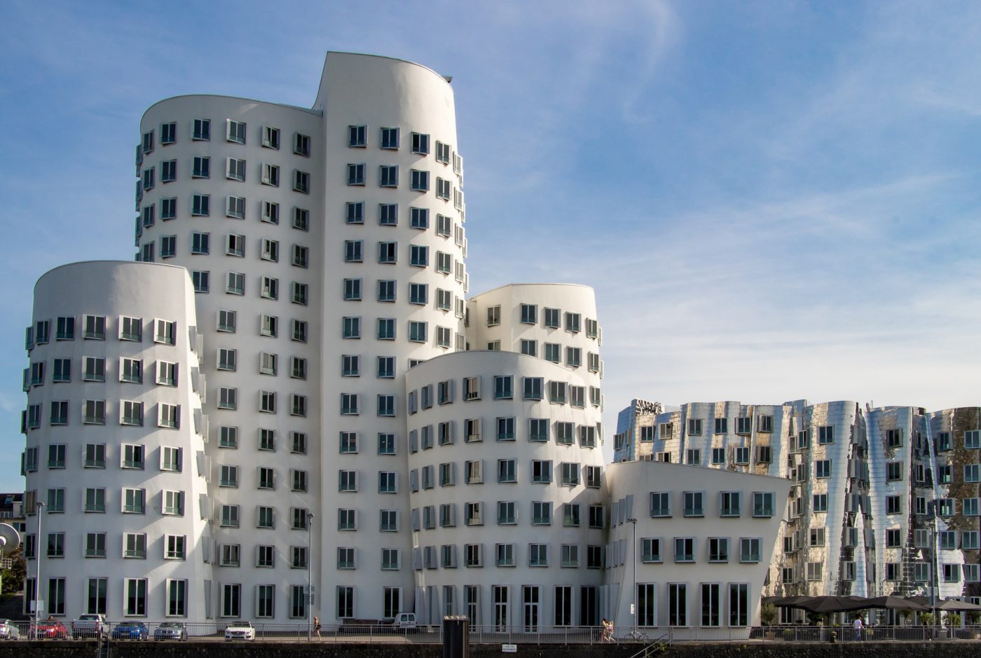 Die geschwungenen weißen und silbernen Gehry-Bauten des Neuen Zollhofs im Düsseldorfer Medienhafen vor blauem Himmel
