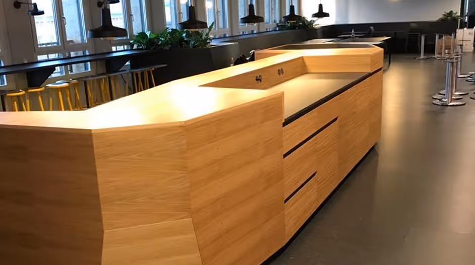 Moderner interner Kantinenbereich mit einer langen Holztheke und schwarzen Pendelleuchten.