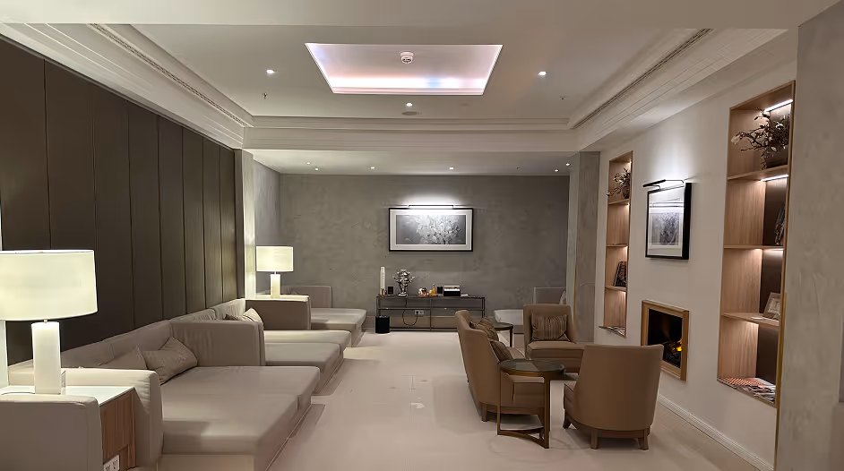 Moderne Lounge mit beigen Sofas, Sesseln, Lampen, Wandbildern und integrierten Regalen an den Wänden.