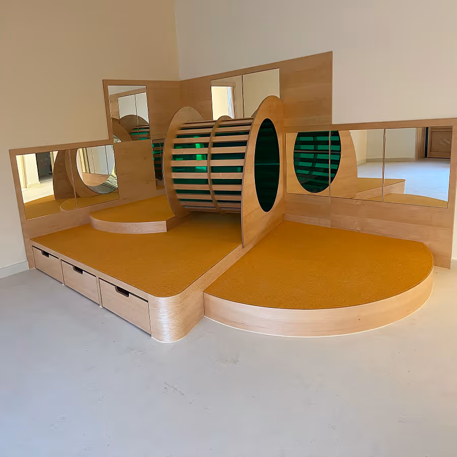 Holzspielplattform mit orangen Teppichbelag, rundem Podest, Tunnel und Spiegelwänden in einem Raum.