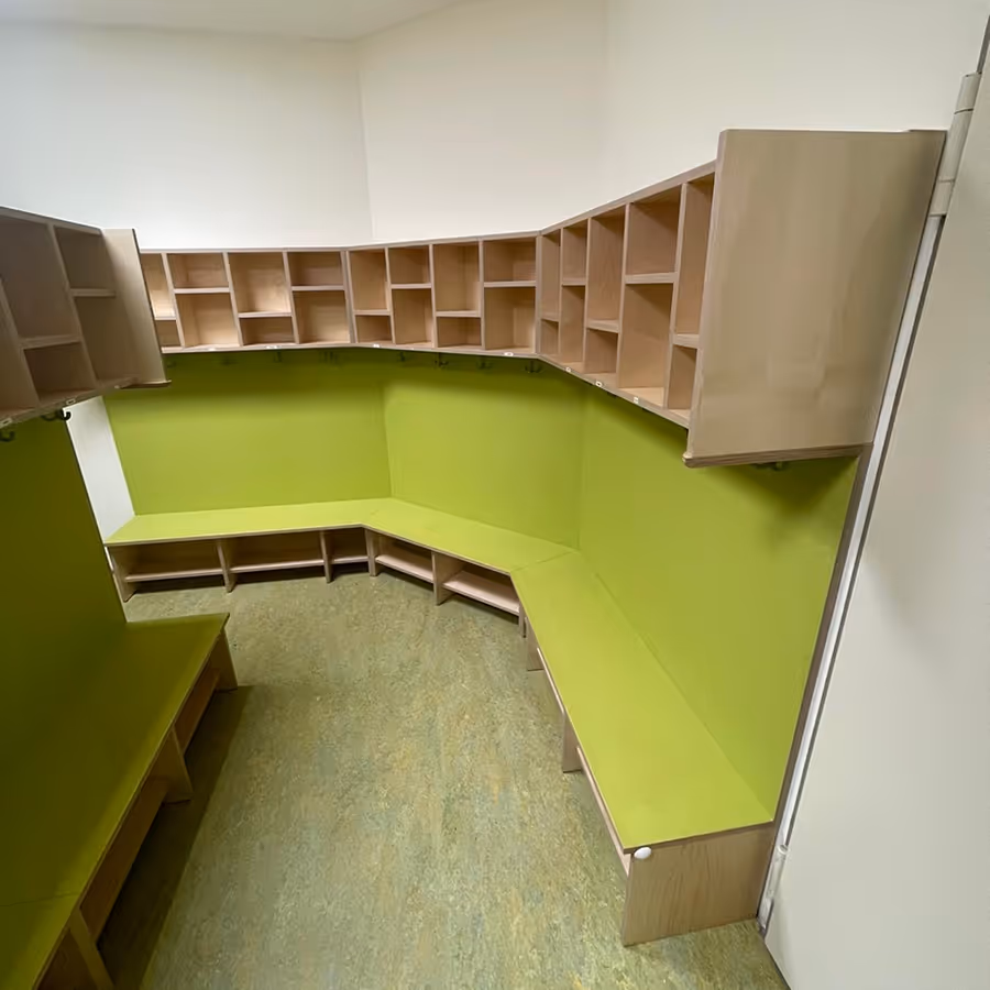 Leerer Raum mit grünen Sitzbänken und hölzernen Wandregalen in einer Ecke.