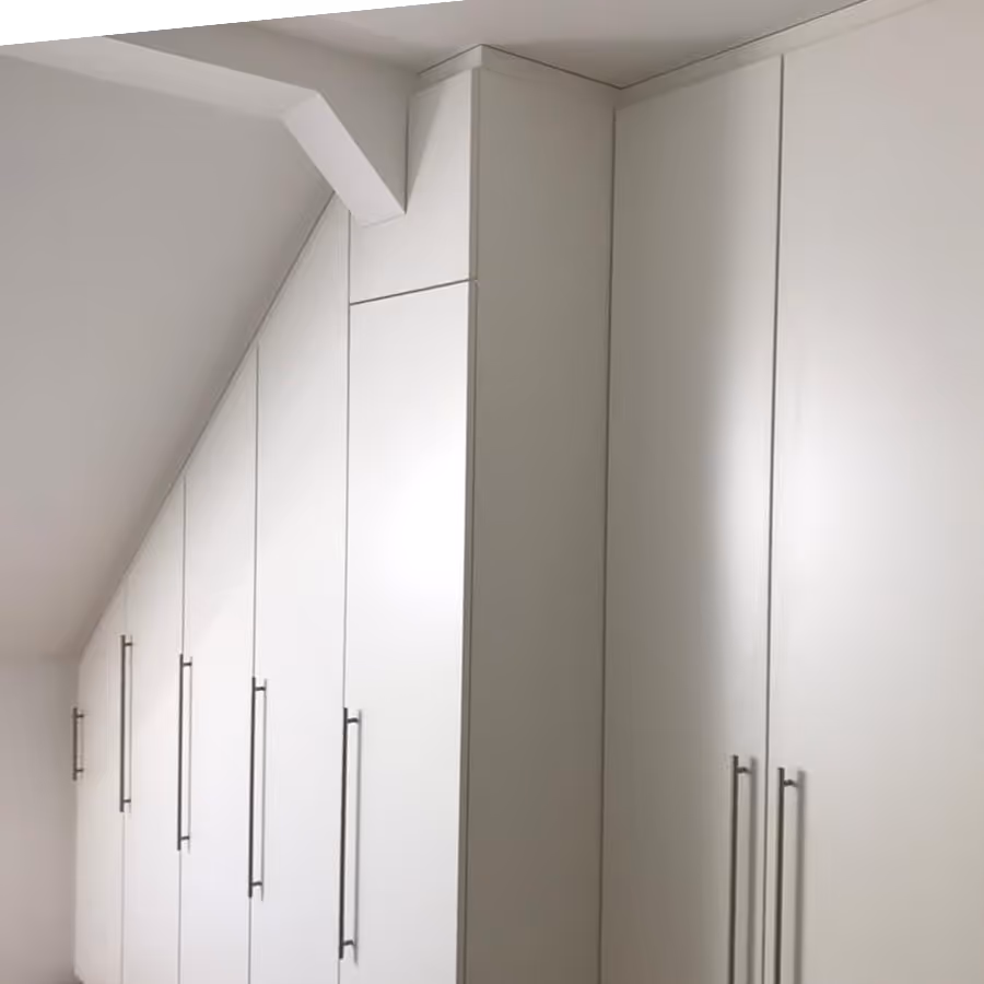 Weiße Einbauschränke mit langen, silbernen Griffen, passend zur schrägen Decke eines Raumes.