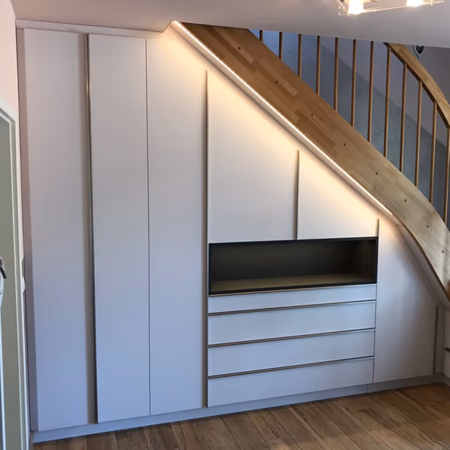 Maßgeschneiderter weißer Einbauschrank unter der Treppe mit Schubladen und offenem Fach, Holztreppe und Holzboden.