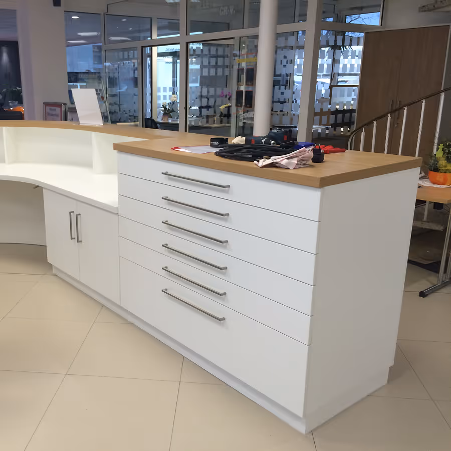 Moderner Empfangstresen mit weißen Schubladen und Holzarbeitsplatte in einem hellen Büro.