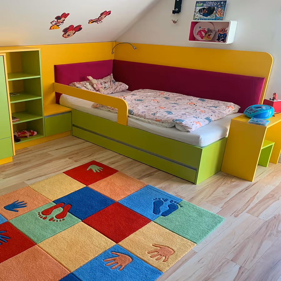 Kinderzimmer mit grün-gelbem Bett und buntem Teppich mit Fuß- und Handabdrücken.