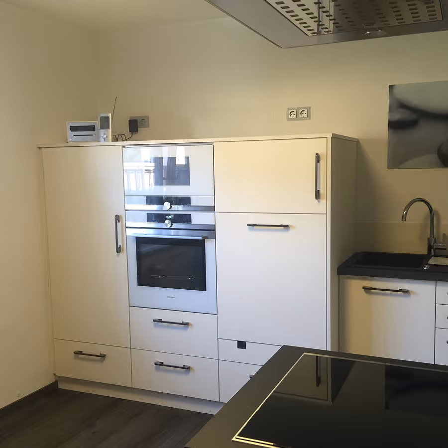 Moderne weiße Einbauküche mit Siemens Ofen, schwarzen Griffen, Spüle und Glaskochfeld.