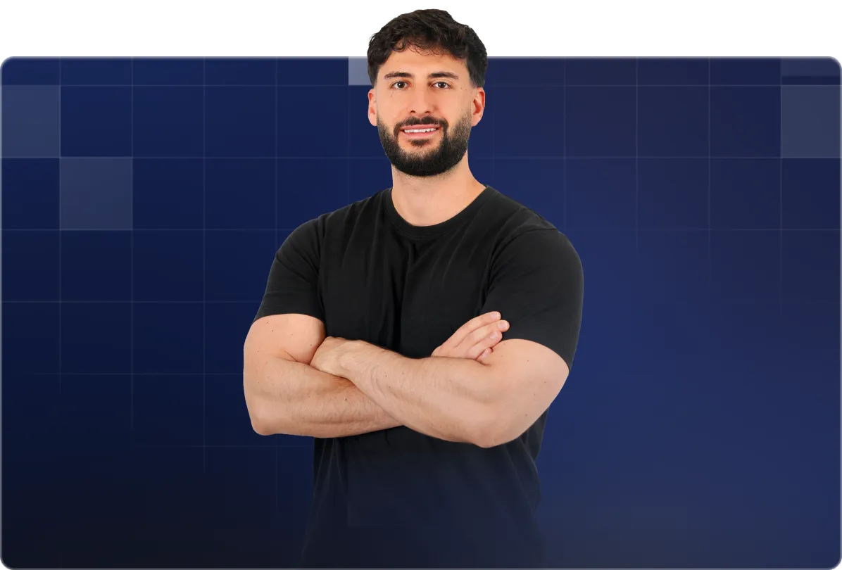 Man with dark hair and beard wearing black shirt with arms crossed, smiling against blue grid background.