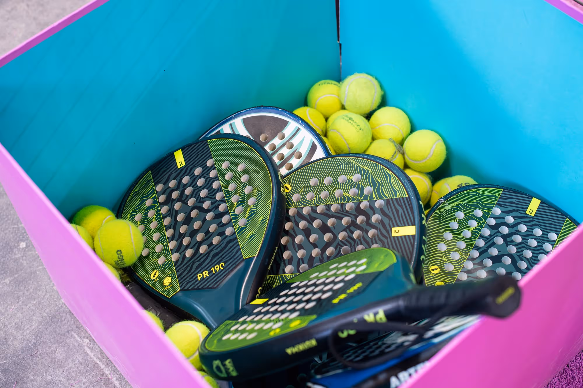 Ein Korb mit grünen und schwarzen Padel-Schlägern und gelben Tennisbällen.